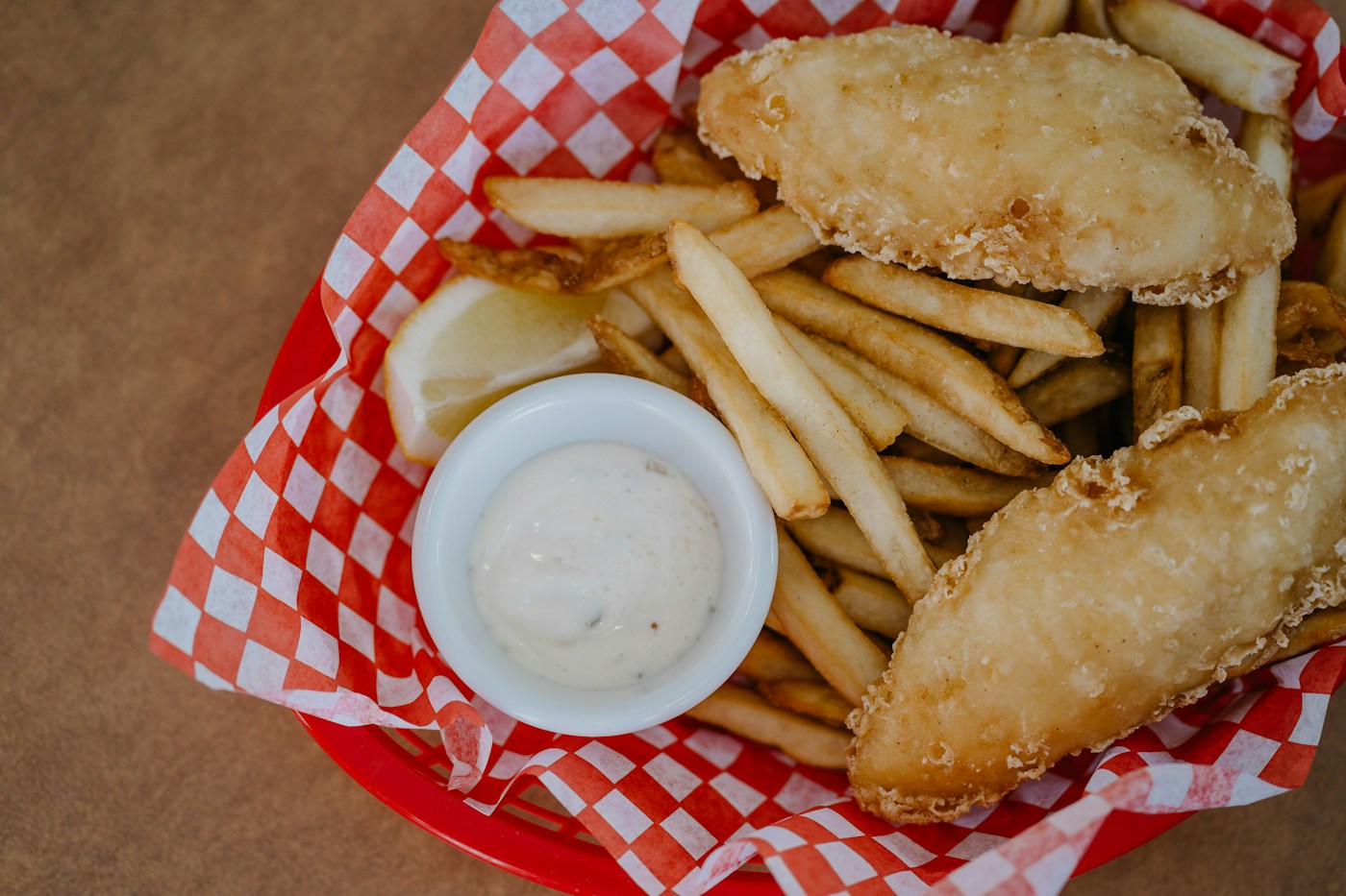 Golden battered fish and thick-cut fries with tartar sauce and lemon in a red-and-white lined basket